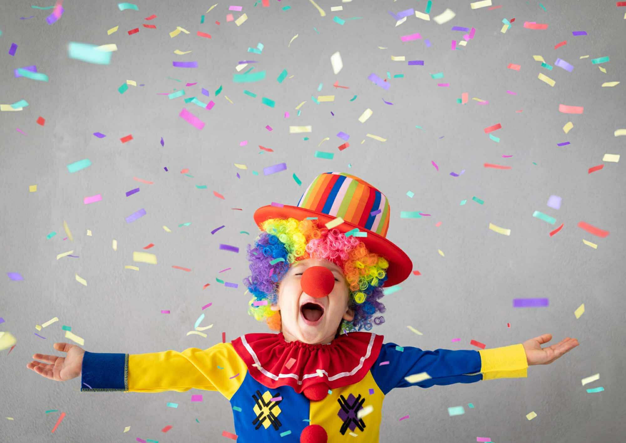 Chłopczyk przebrany za klowna, na kt&oacute;rego spada "deszcz" konfetti.