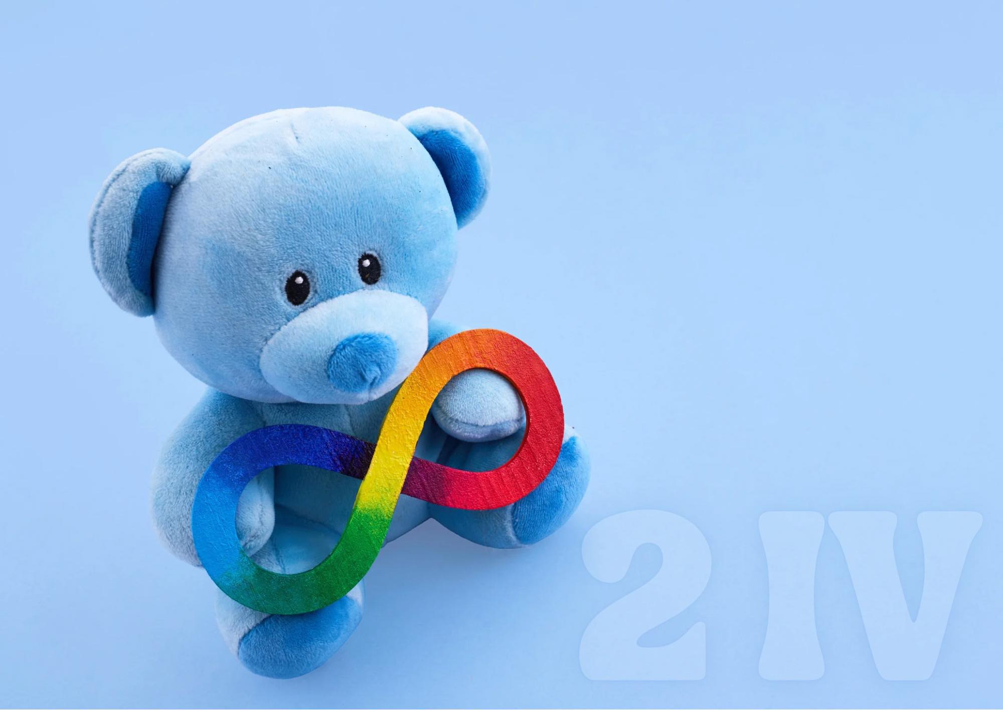 Pluszowy, błękitny miś trzymający znak nieskończoności w kolorach tęczy.