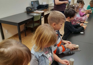 Grupa dzieci wykonuje papierowe jeże, obok nich stoi pani bibliotekarka
