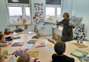 Dzieci opowiadają co widzą na obrazku w książce, który pokazuje im pani bibliotekarka.