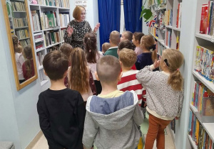Grupa dzieci stoi i słucha opowieści pani bibliotekarki