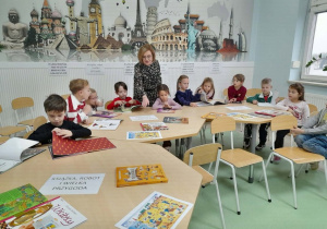 Grupa dzieci siedzi przy stolikach i ogląda książki