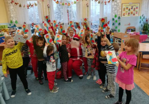 Zdjęcie grupowe z Mikołajem, dzieci prezentują otrzymane książeczki.
