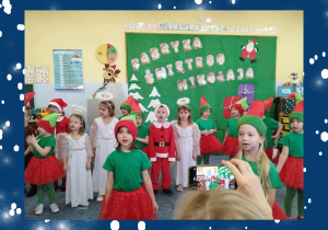 Grupa dzieci w świątecznych przebraniach podczas występu bożonarodzeniowego.