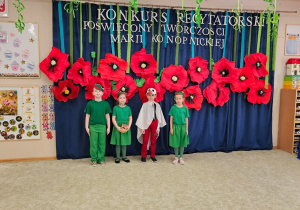 Grupa dzieci w przebraniach podczas recytacji wiersza, w tle dekoracja - duże, czerwone maki.