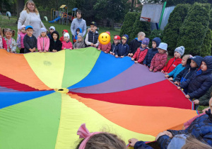 Grupa dzieci trzyma kolorową chustę animacyjną.