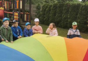 Grupa dzieci trzyma kolorową chustę animacyjną.