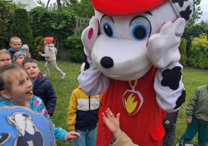 Dzieci otaczają dużego psa - strażaka (chodzącą maskotkę).