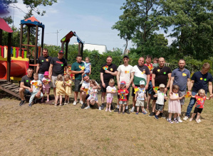 Tatusiowie i dzieci w ogrodzie przedszkolnym pozują do grupowego zdjęcia.