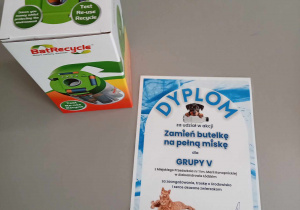 Zdjęcie otrzymanego dyplomu i nagrody w postaci pojemnika na zużyte baterie.