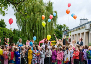 Grupa osób patrząca na odlatujące kolorowe balony.