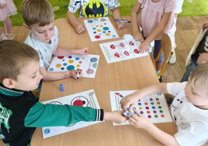 Grupa dzieci siedzi przy stoliku i rozwiązuje zadania.