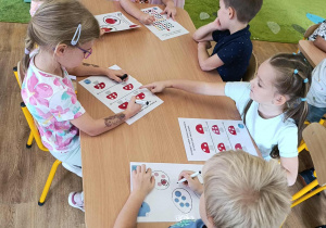 Grupa dzieci siedzi przy stoliku i rozwiązuje zadania.
