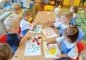 Dzieci przy stoliku tworzą swoje kropkowe obrazki