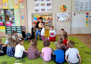 Dzieci siedzą w kręgu na dywanie i słuchają czytanej przez mamę Lilianki książki