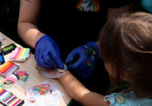 Dziecko w trakcie wykonywania "tatuażu" z brokatu przez animatorkę.
