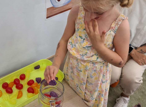 Dziewczynka wrzuca kolorowe owoce do dzbanka z wodą.