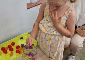 Dziewczynka wrzuca kolorowe owoce do dzbanka z wodą.