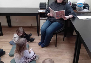 Pani Bibliotekarką siedząc na krześle czyta opowiadania o jesieni.