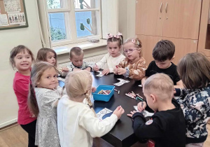 Dzieci stoją wokół stołu i kolorują obrazki kaloszy.