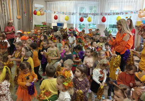 Dzieci (w jesiennych przebraniach) bawią się błyszczącymi pomponami na Balu Jesieni.