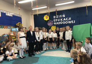 Grupa dzieci (w eleganckich, galowych strojach) podczas prezentacji skeczu z okazji Dnia Nauczyciela.