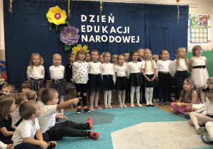 Grupa dzieci (w eleganckich, galowych strojach) podczas występu z okazji Dnia Nauczyciela.