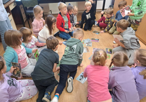 Grupa dzieci siedzi w kole na podłodze i wyszukuje wśród rozłożonych obrazków, ilustrację związane z jesienią.