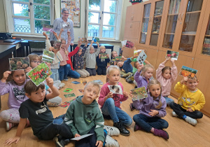 Grupa dzieci siedzi w kole na podłodze i wyszukuje wśród rozłożonych obrazków, ilustrację związane z jesienią.