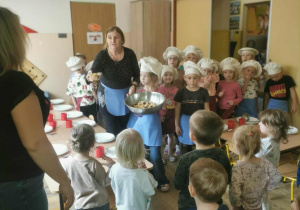 Grupa dzieci częstuje młodszych kolegów z przedszkola wykonaną przez siebie sałatką.