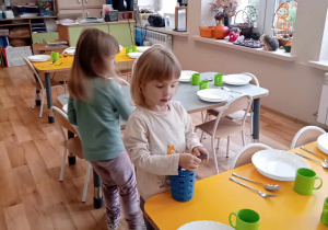 Dwie dziewczynki rozkładają widelce przy talerzach.