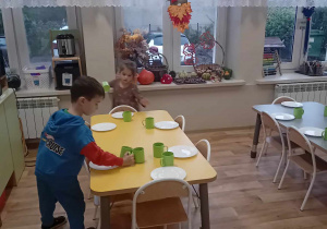 Chłopiec rozkłada przy każdym talerzu kubeczki do kompotu.