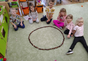 Grupka dzieci z ułożoną z kasztanów literką "O".