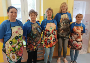Grupa pań w niebieskich podkoszulkach i fartuszkach z kolorowymi nadrukami.