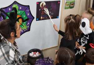 Dziewczynka wskazuje ukryty element na obrazku za pomocą ręki szkieletora.