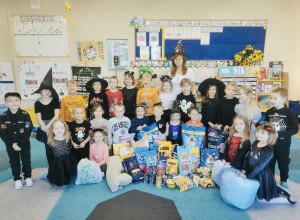 Grupa przedszkolaków wraz z nauczycielką pozuje do zdjęcia z zebraną przez siebie karmą dla schroniska.