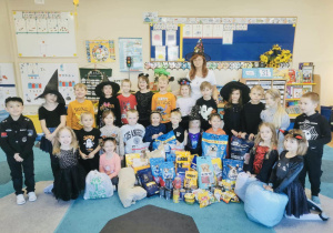 Grupa przedszkolaków wraz z nauczycielką pozuje do zdjęcia z zebraną przez siebie karmą dla schroniska.