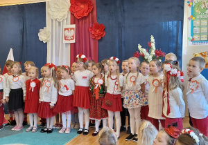Grupa dzieci w biało-czerwonych strojach podczas śpiewania patriotycznej piosenki..