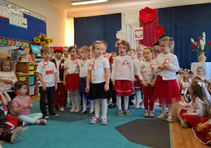 Grupa dzieci w biało-czerwonych strojach podczas śpiewania patriotycznej piosenki..