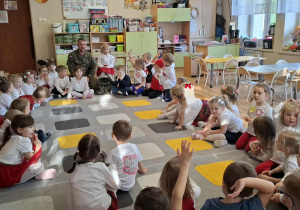 Żołnierz opowiada (siedzącym na dywanie dzieciom) o swojej pracy.