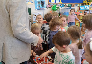 Pan Burmistrz częstuje dzieci słodyczami z wiklinowego kosza.