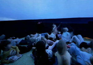Przedszkolaki podziwiają film, wyświetlany na powierzchni sferycznej kopuły.