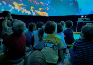 Przedszkolaki podziwiają film, wyświetlany na powierzchni sferycznej kopuły.