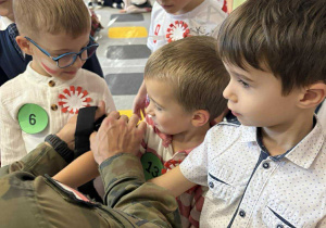 Żołnierz "zakłada" dziecku opaskę uciskową.