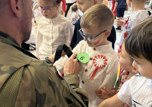 Żołnierz "zakłada" dziecku opaskę uciskową.