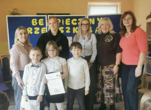 Troje uczestników konkursu z nagrodą i dyplomem za I miejsce w konkursie pozują do zdjęcia w towarzystwie jury i nauczycielki grupy.