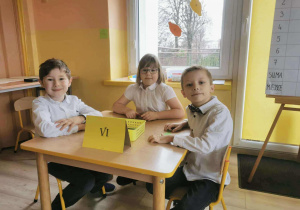 Troje dzieci siedzi przy stoliku w oczekiwaniu na zadanie konkursowe.