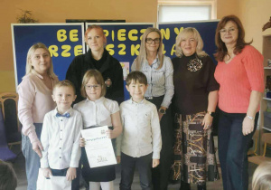 Troje uczestników konkursu z nagrodą i dyplomem za I miejsce w konkursie pozują do zdjęcia w towarzystwie jury i nauczycielki grupy.