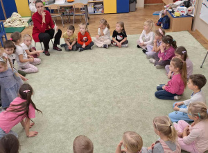 Dzieci (zgromadzone w kole na dywanie) podczas zajęć z pedagogiem i psychologiem.