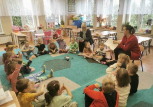 Dzieci (zgromadzone w kole na dywanie) podczas zajęć z pedagogiem i psychologiem.